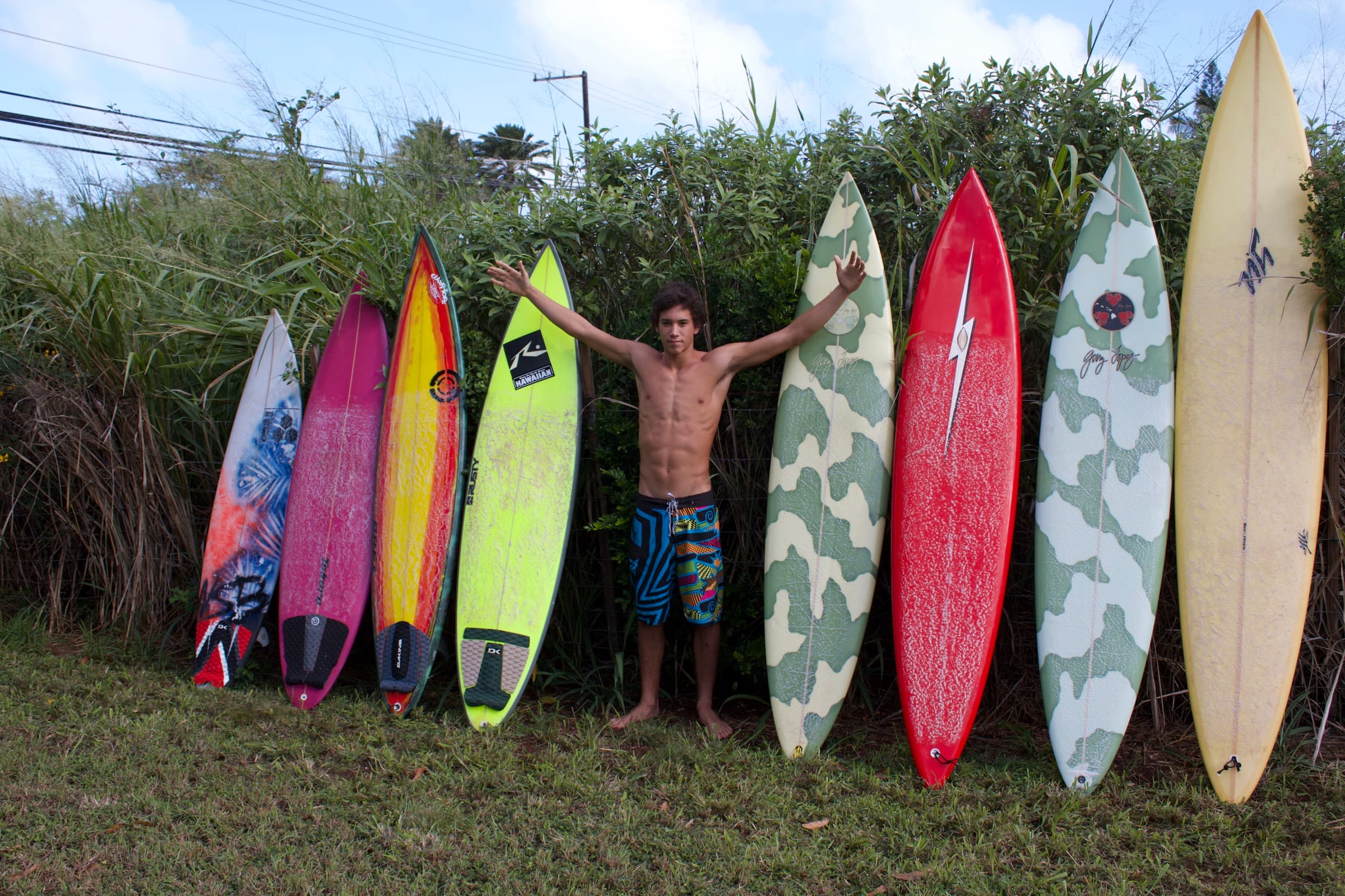 A surfer standing in a row of custom surfboards